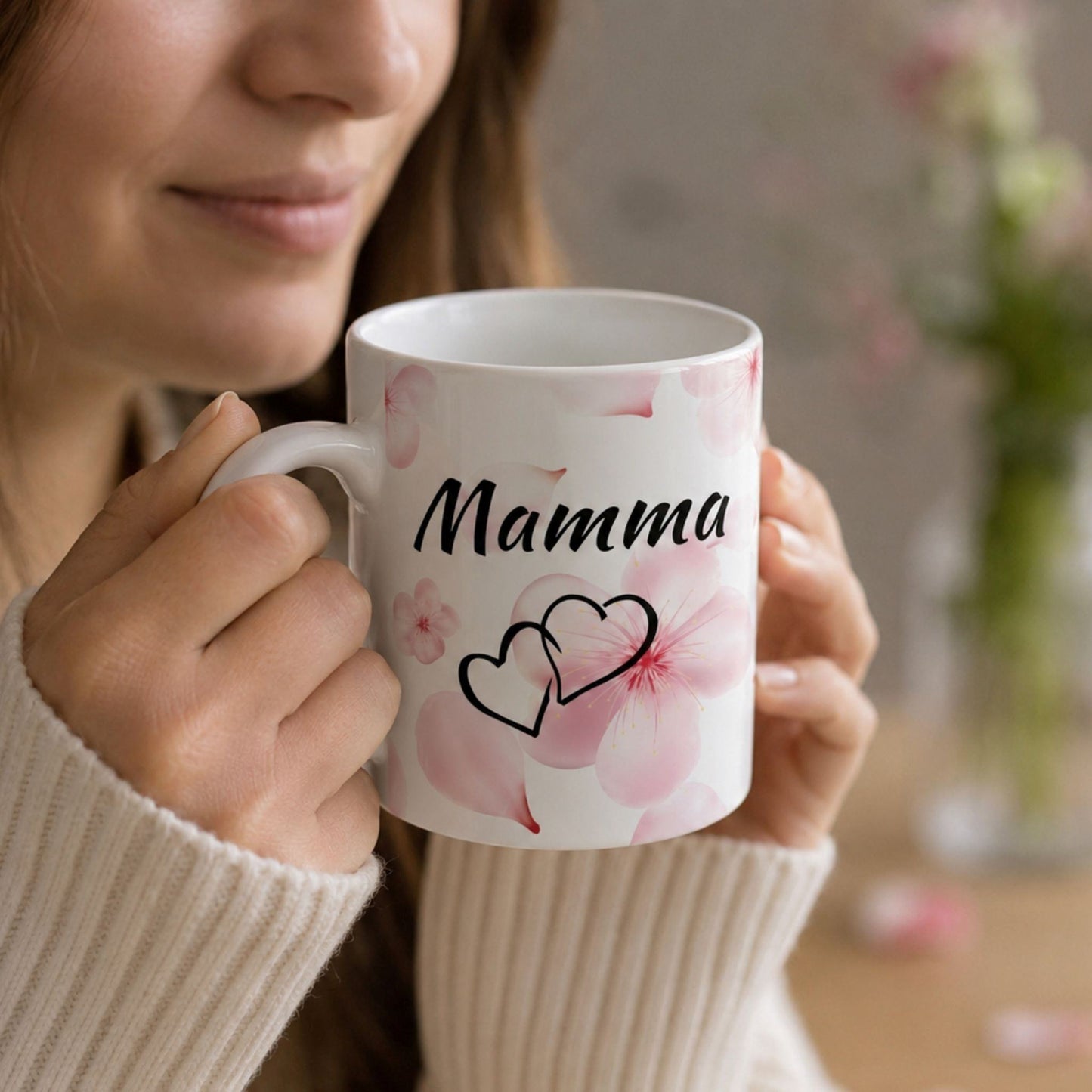Sieviete mājīgā džemperī tur rokās krūzi ar uzrakstu "Mamma", radot siltu un profesionālu zīmola koptēlu "klusā luksusa" noskaņās.