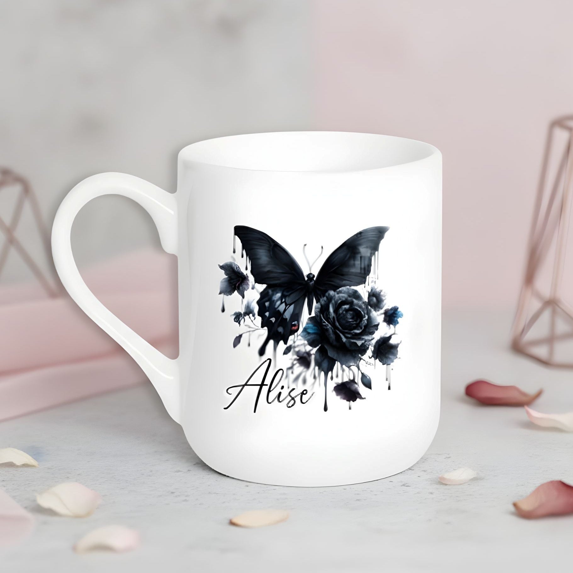 Balta keramikas krūze ar melna tauriņa un rozes ilustrāciju un personalizētu vārdu.