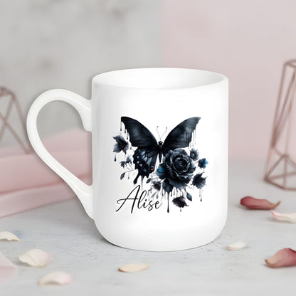 Balta keramikas krūze ar melna tauriņa un rozes ilustrāciju un personalizētu vārdu.