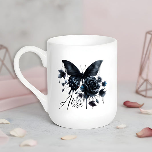 Balta keramikas krūze ar melna tauriņa un rozes ilustrāciju un personalizētu vārdu.
