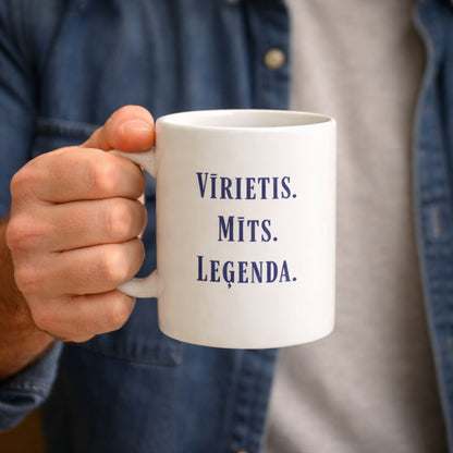 Vīrietis tur rokā baltu keramikas krūzi ar uzrakstu "Vīrietis. Mīts. Leģenda."