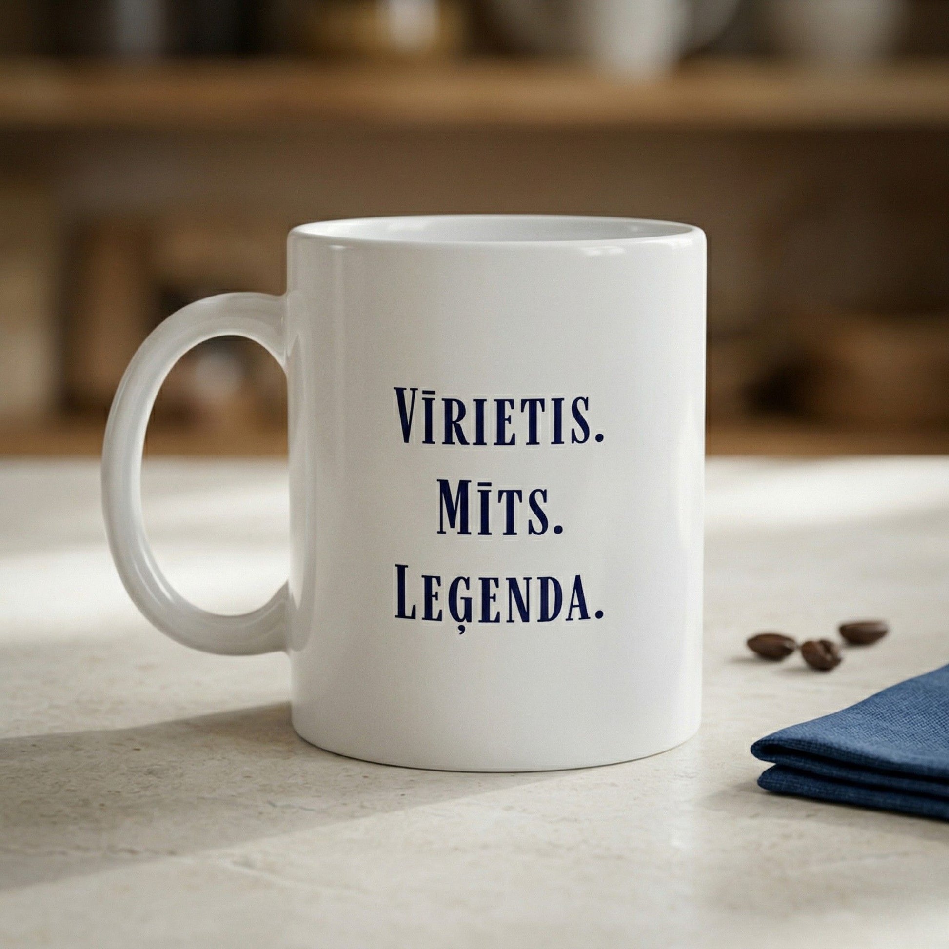 Balta keramikas krūze ar uzrakstu "Vīrietis. Mīts. Leģenda." uz gaiša virtuves fona