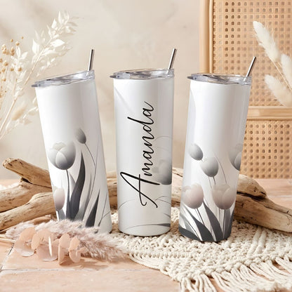 Trīs baltas 20oz termokrūzes ar minimālistisku tulpju zīmējumu pelēkos un rozā toņos, vidējā krūze personalizēta ar vārdu "Amanda" elegantā kaligrāfijas rakstā.