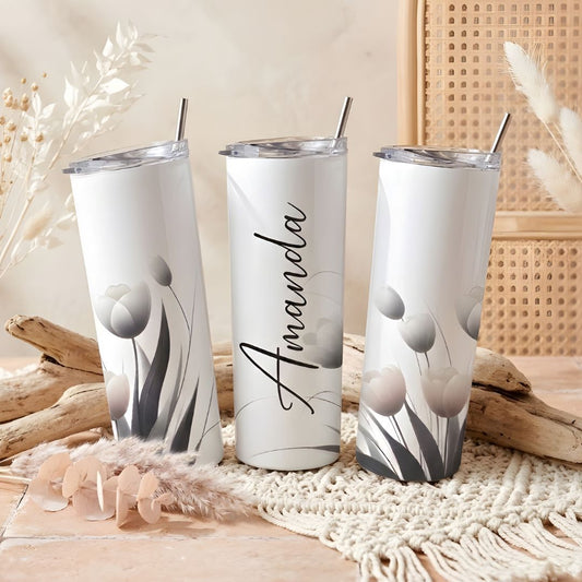 Trīs baltas 20oz termokrūzes ar minimālistisku tulpju zīmējumu pelēkos un rozā toņos, vidējā krūze personalizēta ar vārdu "Amanda" elegantā kaligrāfijas rakstā.