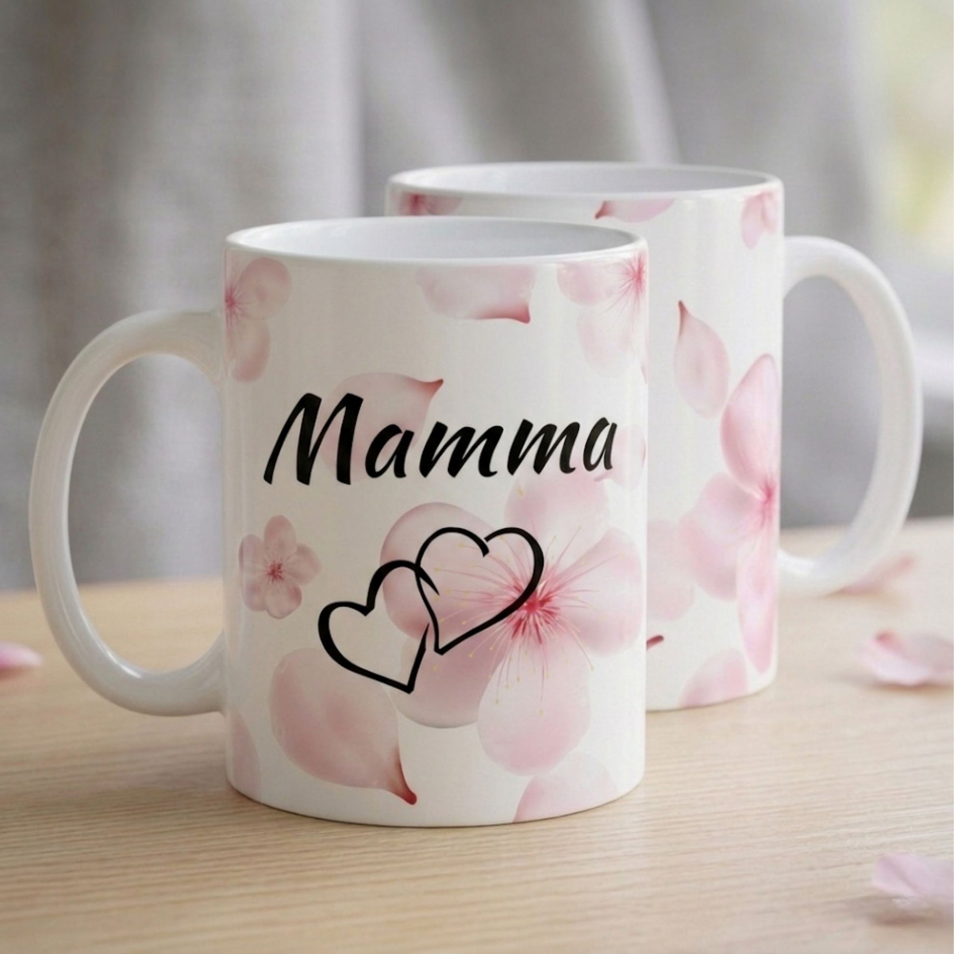 Divas baltas krūzes novietotas viena aiz otras, parādot gan priekšpuses uzrakstu "Mamma", gan estētisko ziedu rakstu no abām pusēm.