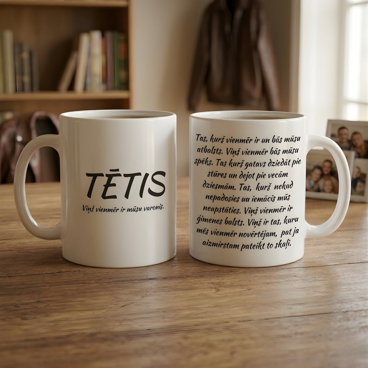 Divas baltas keramikas krūzes blakus viena otrai, parādot gan priekšpuses uzrakstu "TĒTIS", gan aizmugures dzejoli reālistiskā mājas interjerā.