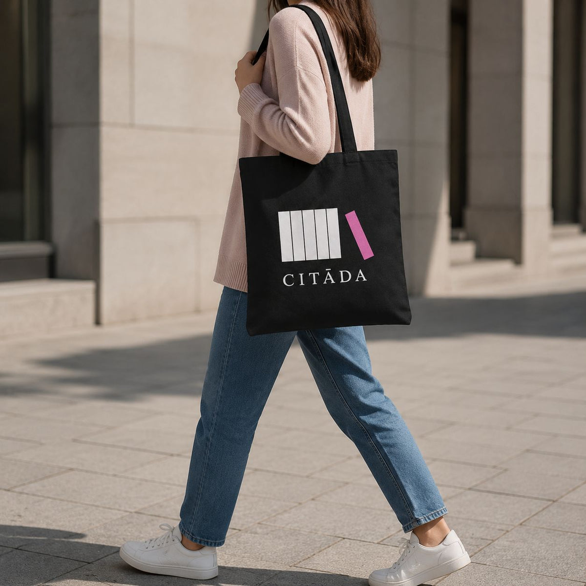 Sieviete ikdienā nes melnu 34 × 38 cm kanvas somu ar uzrakstu “Citāda”