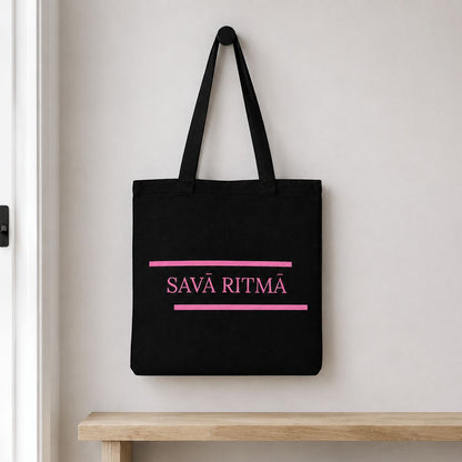 Melna kanvas soma “Savā ritmā” pie sienas gaišā priekšnamā.