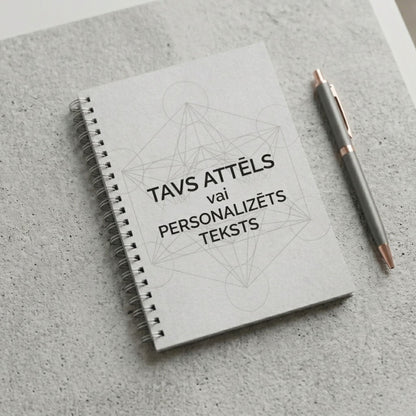 Minimālistiska pelēka piezīmju klade ar spirāli un uzrakstu "Tavs attēls vai personalizēts teksts" uz betona tekstūras fona ar pildspalvu.