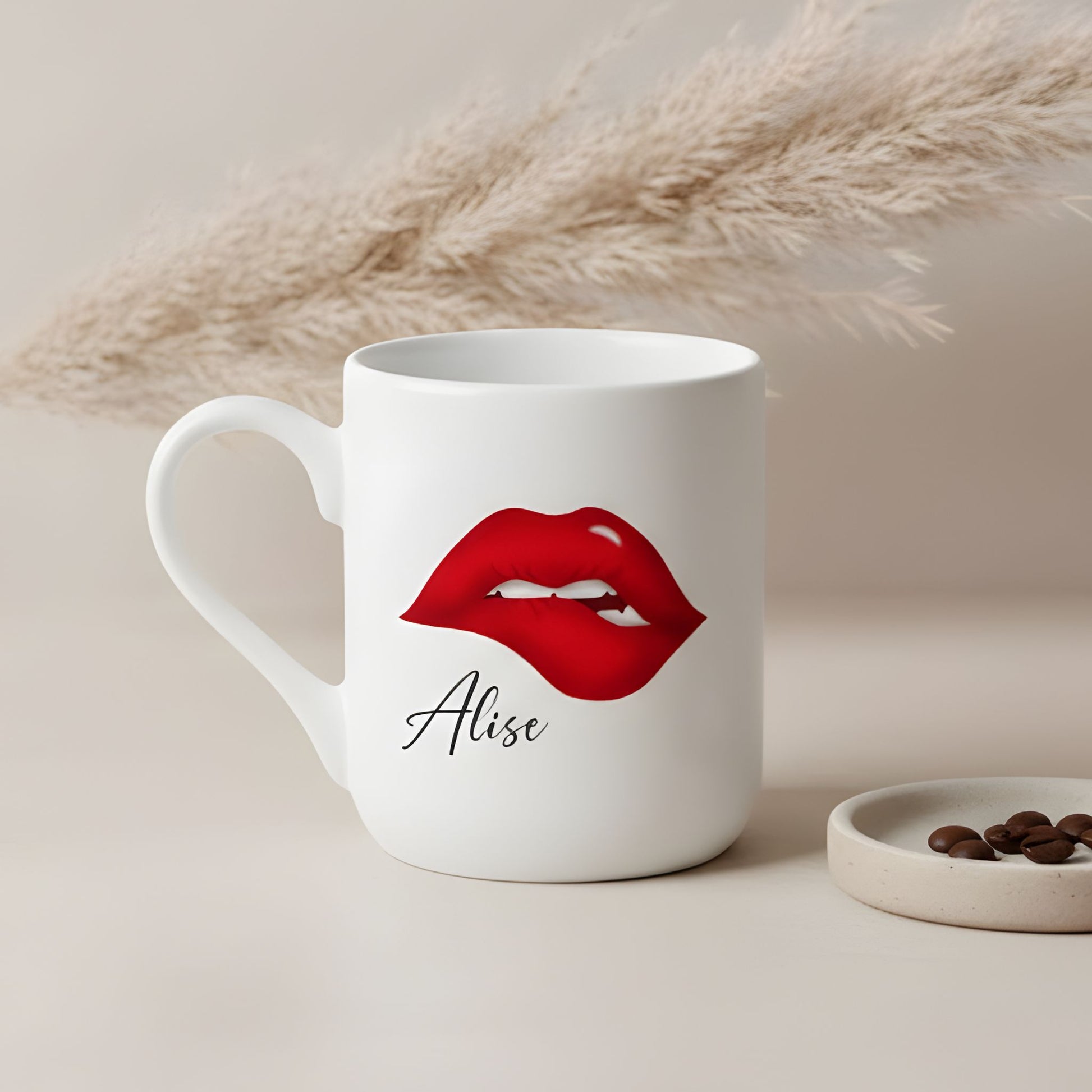 Personalizēta balta keramikas krūze ar lūpu dizainu un vārdu uz estētiska bēša fona ar dekoratīvu sauso ziedu.