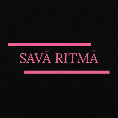 Rozā uzraksta “Savā ritmā” tuvplāns uz izturīgas melnas kanvas somas.